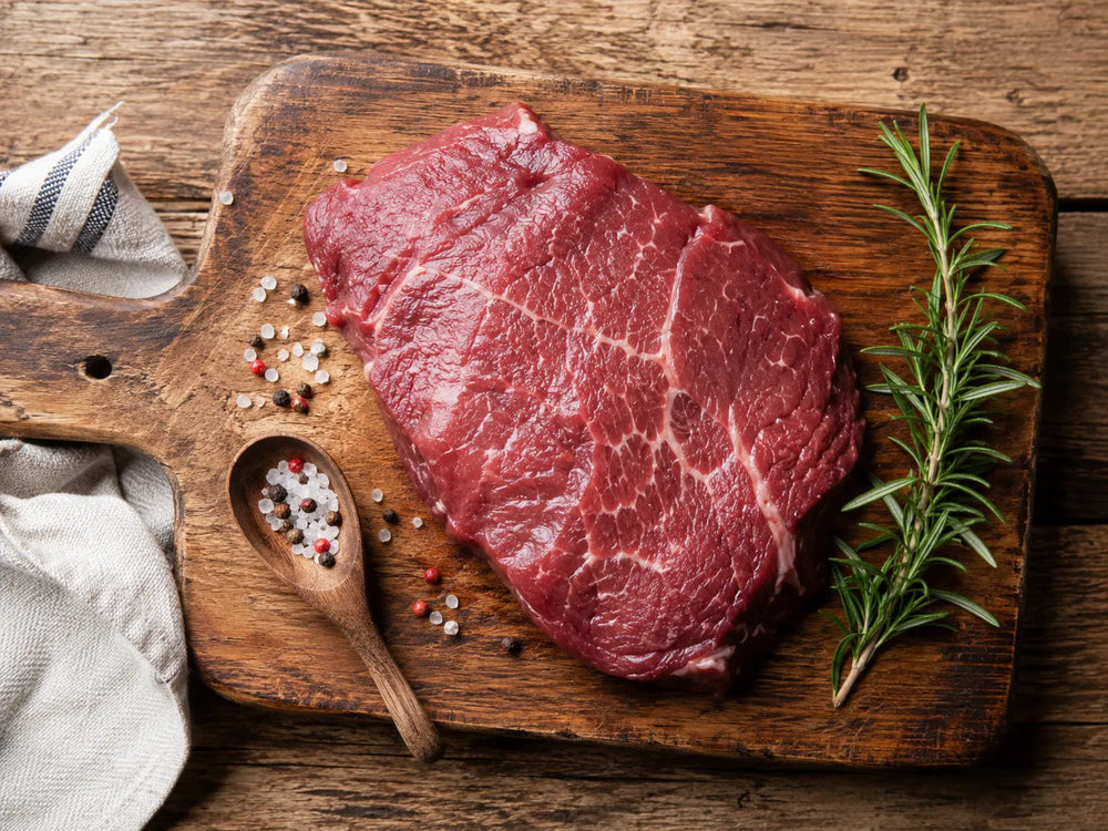 Raw beef cut on a wooden cutting board with fresh rosemary